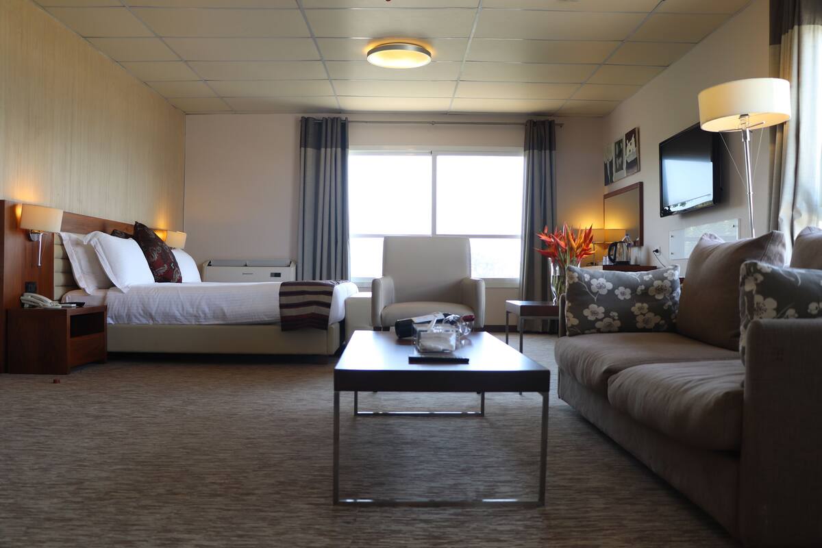 A hotel room with a bed, a sofa, a coffee table, and a TV.