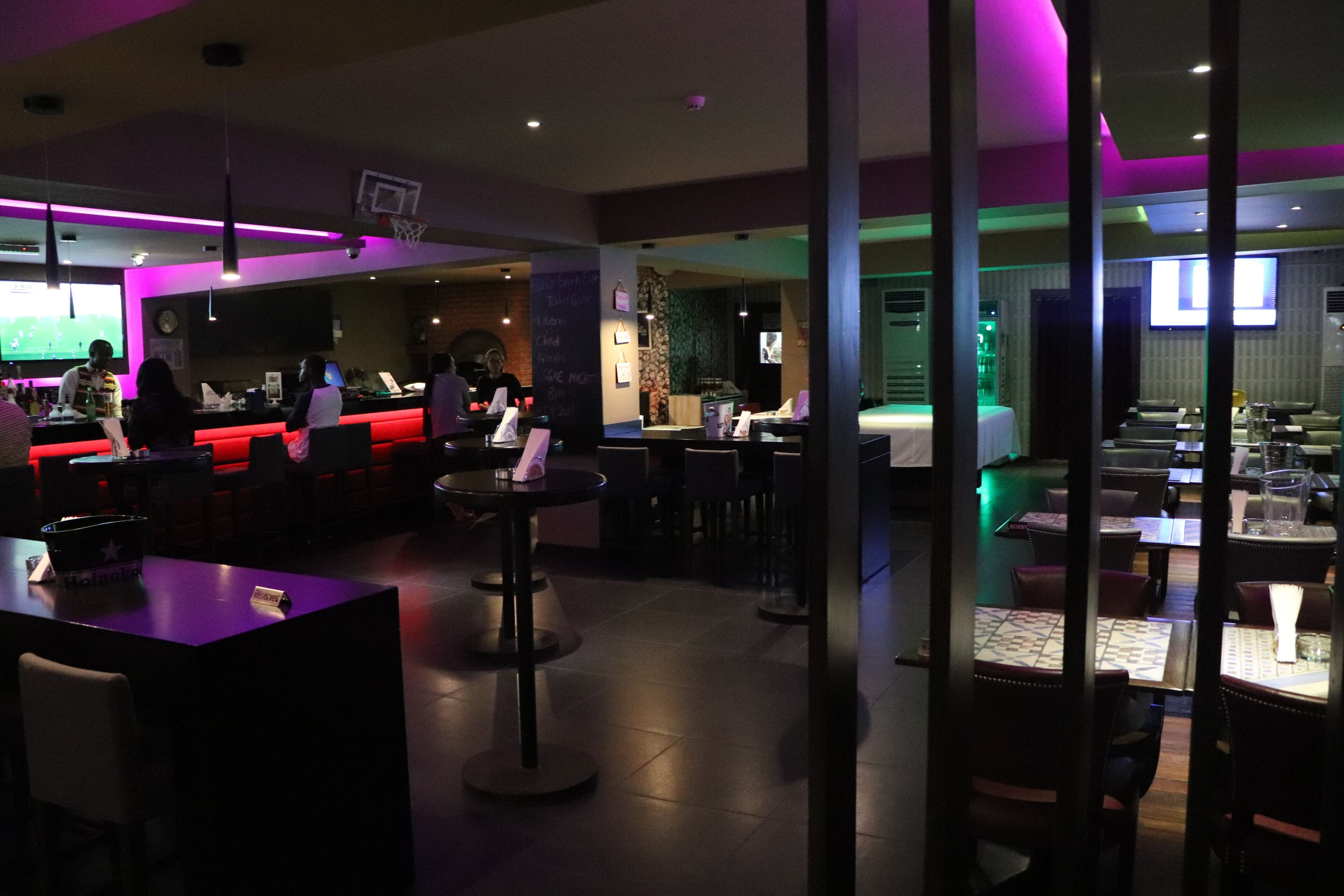 A dimly lit restaurant with tables and chairs, a bar area, and a counter with a menu board.