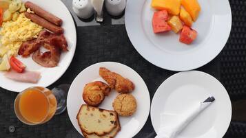 A breakfast setting with plates of eggs, bacon, sausages, and toast, along with a glass of orange juice.