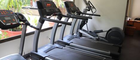 Ein Fitnessraum mit Laufbändern und Trainingsgeräten, ein Fenster mit Blick auf Grünflächen und eine Tür zu einem weiteren Raum.