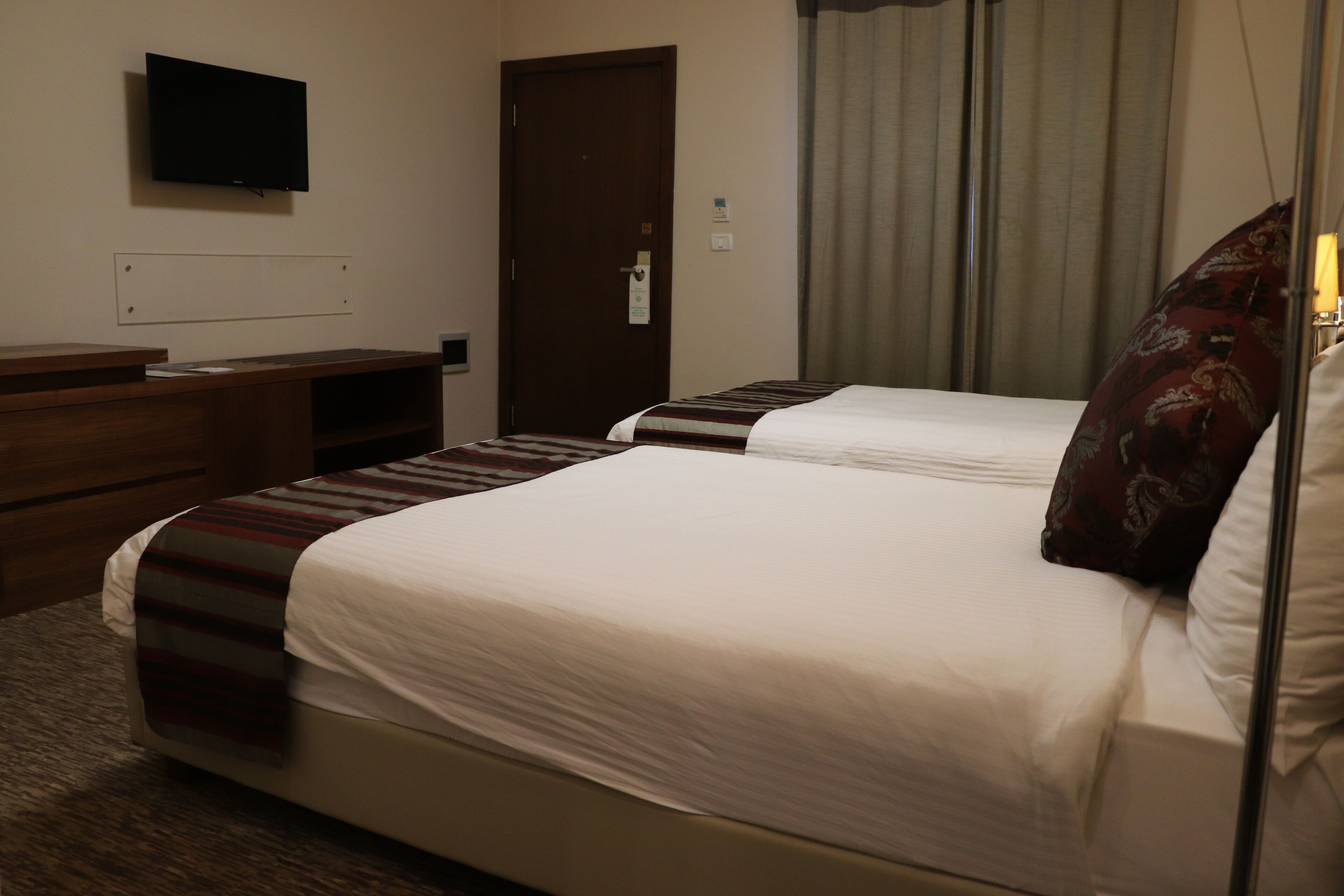 A hotel room with two beds, a television on the wall, a desk, and a door.