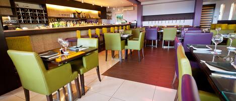 Un interior de restaurante moderno con varias mesas y sillas, una zona de bar con estantes llenos de botellas y un suelo de baldosas impecable.
