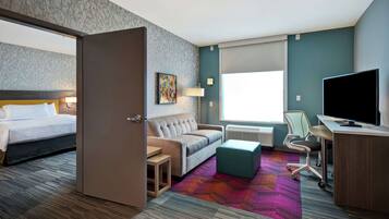 A hotel room with a bed, sofa, desk, TV, and a colorful carpet.