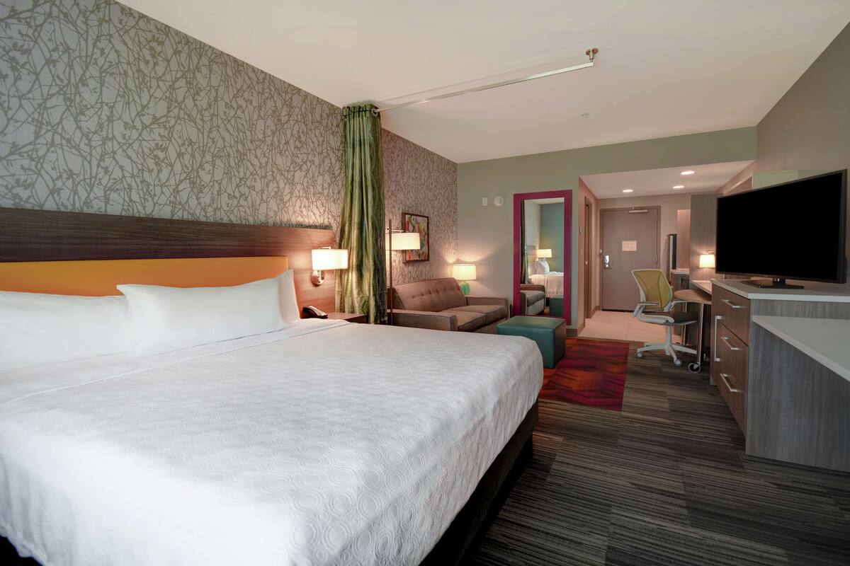 Une chambre d’hôtel avec un grand lit, un bureau doté d’un téléviseur à écran plat, un canapé et une petite table.