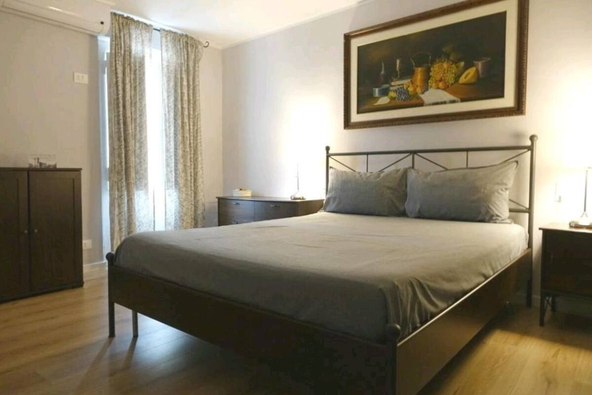 A bedroom with a bed, a nightstand, a dresser, and a painting on the wall.