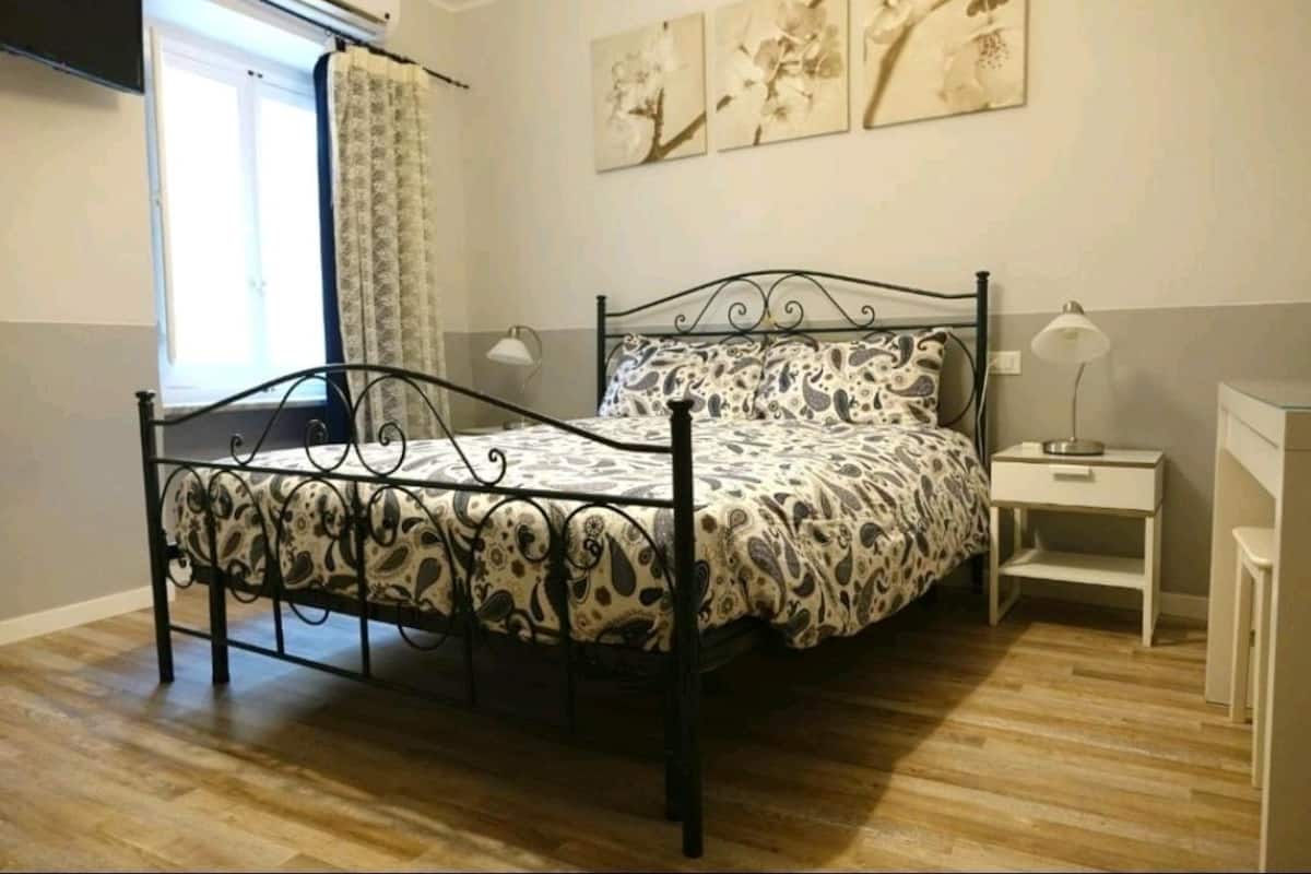 A bedroom with a bed, a bedside table, a lamp, and a window with curtains.