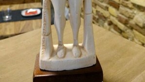 Una estatua blanca de un hombre con sombrero, sobre un pedestal de madera.