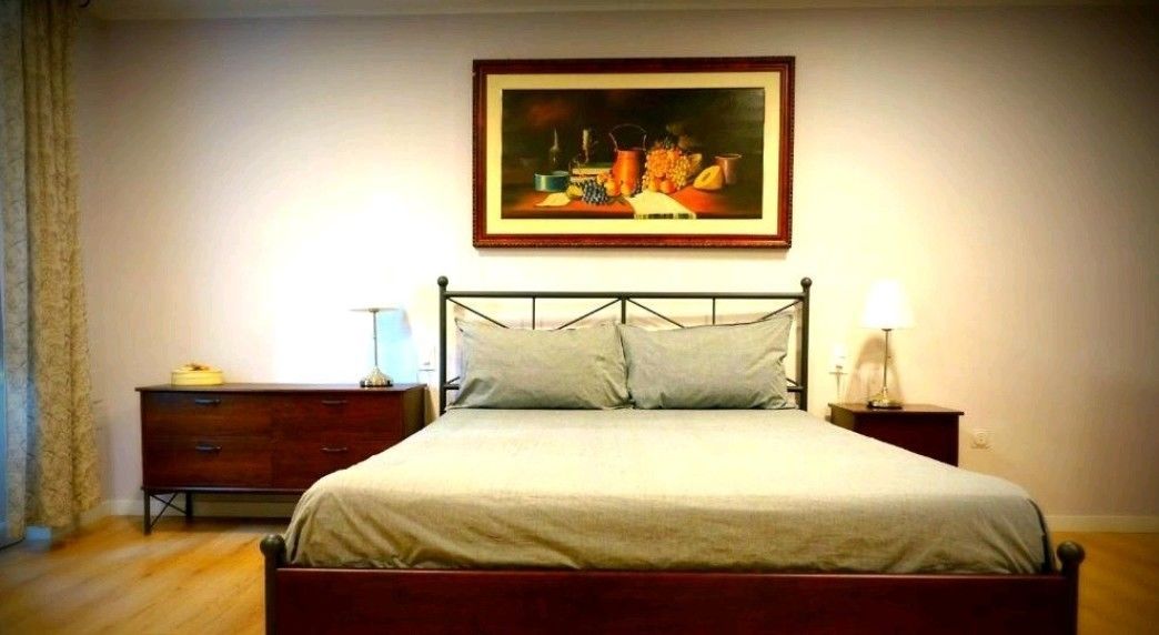 A bedroom with a bed, a nightstand, a dresser, and a painting on the wall.
