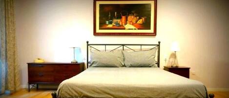 A bedroom with a bed, a nightstand, a dresser, and a painting on the wall.