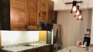 A modern kitchen with wooden cabinets, a stainless steel refrigerator, a built-in oven, and a marble island with a sink. - Modern studio in Puerto Vallarta Down Town (Puerto Vallarta)