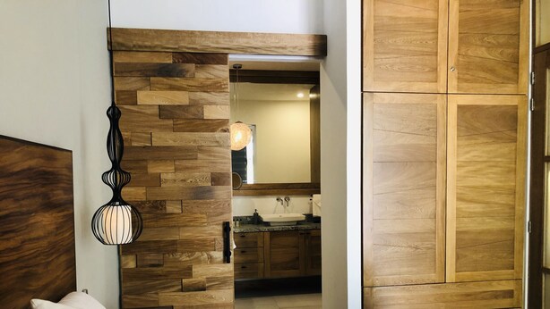 A bedroom with a wooden headboard, a bedside lamp, a bed with white bedding, and a view into the bathroom. - Modern studio in Puerto Vallarta Down Town (Puerto Vallarta)