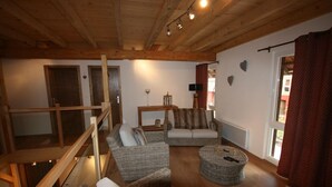 Una sala de estar acogedora con techo de madera, un conjunto de sofás, una mesa de centro redonda y una escalera.