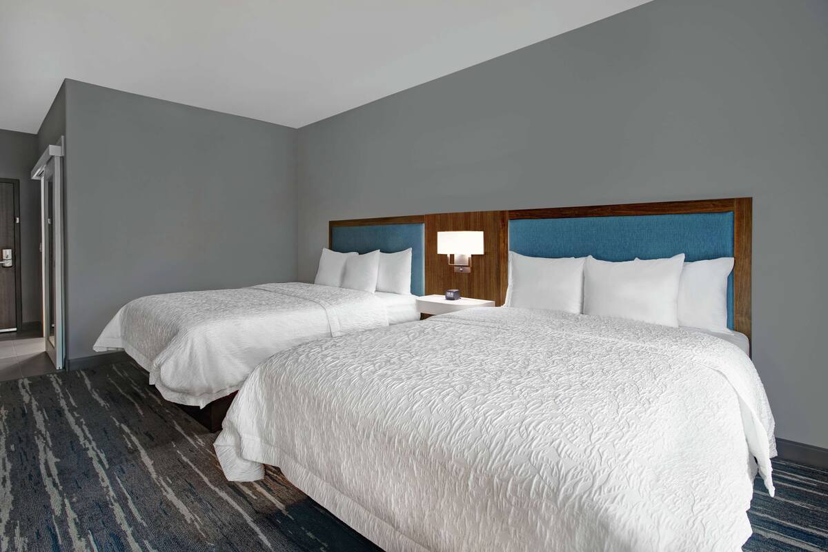 A hotel room with two single beds, a small bedside table with a lamp, and a patterned rug.
