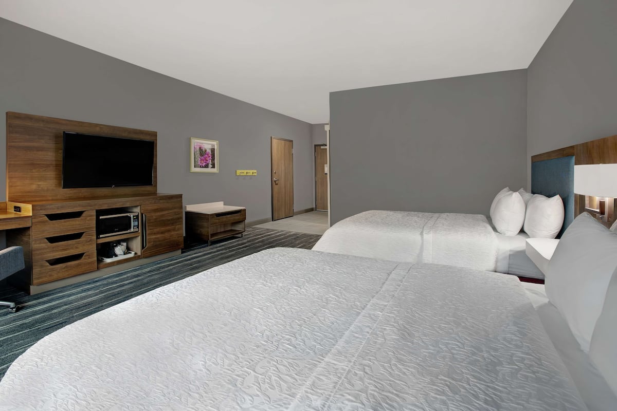 A hotel room with two beds, a TV on a wooden stand, a desk with drawers, and a small table.