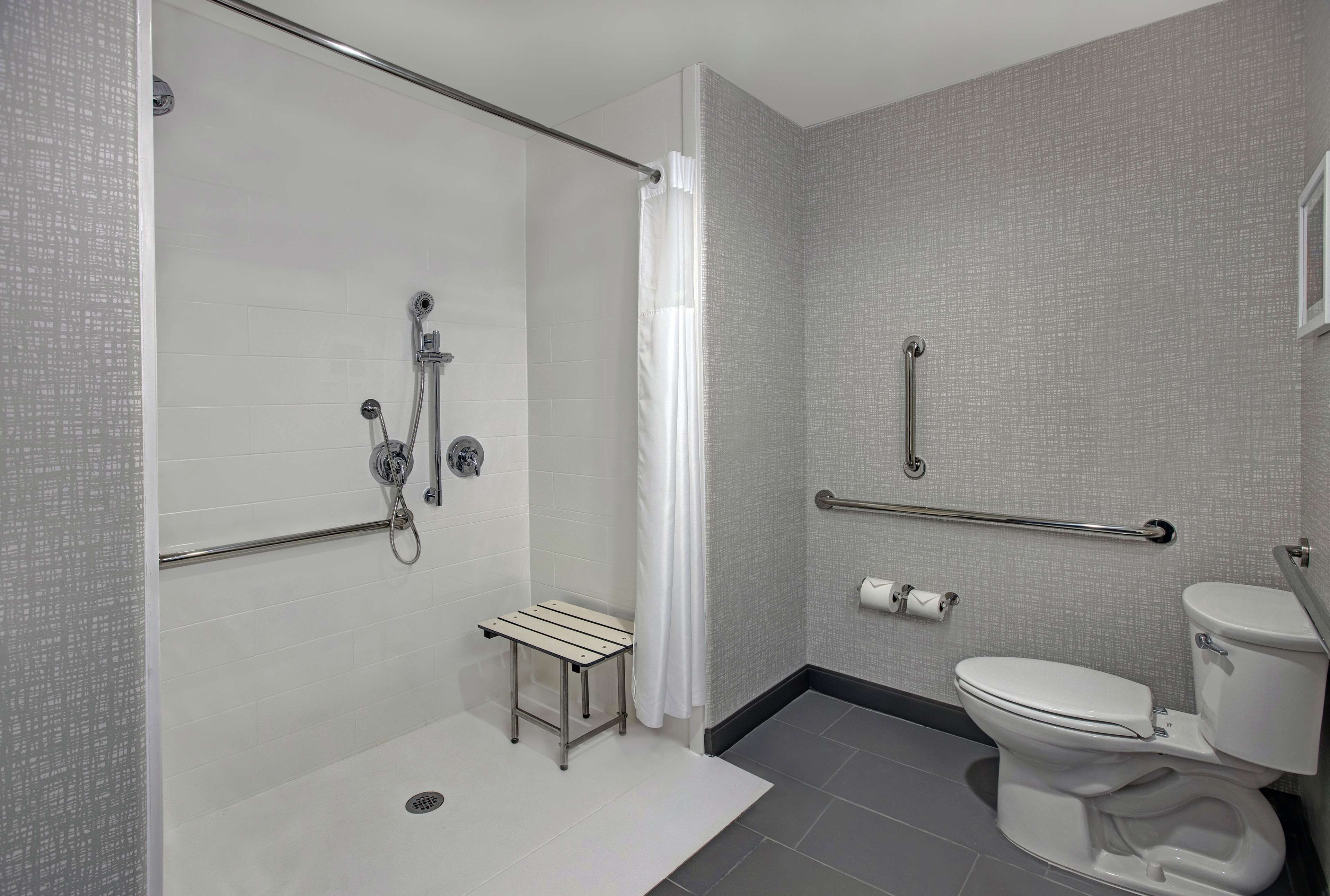 Ein modernes Badezimmer mit begehbarer Dusche, Haltegriffen, Toilette und einer kleinen Sitzbank.