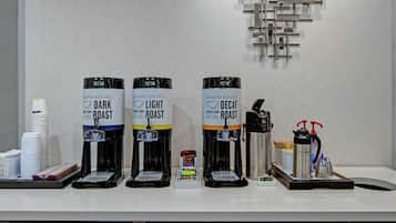 Three coffee machines labeled DARK ROAST, LIGHT ROAST, and DECAF on a counter with stacks of white plates and a coffee grinder.