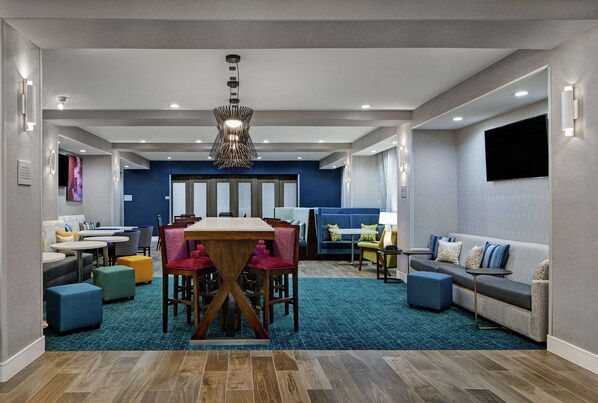 A modern hotel lobby with a dining area, seating, and a TV wall. - Hampton Inn Weslaco (Weslaco)