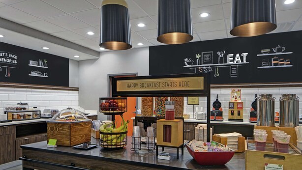 A breakfast buffet area with various food items and a sign that reads "HAPPY BREAKFAST STARTS HERE". - Hampton Inn Weslaco (Weslaco)