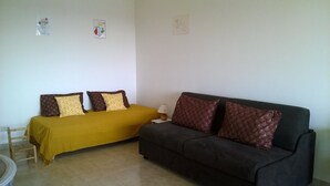 A room with a bed and a sofa, both with patterned cushions, a small table with a lamp, and a chair. - ANTIBES - LARGE STUDIO BRIGHT, SEA VIEW for 4 pers (Antibes)