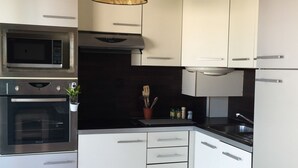 A modern kitchen with white cabinets, a microwave, oven, and a hanging light fixture. - ANTIBES - LARGE STUDIO BRIGHT, SEA VIEW for 4 pers (Antibes)