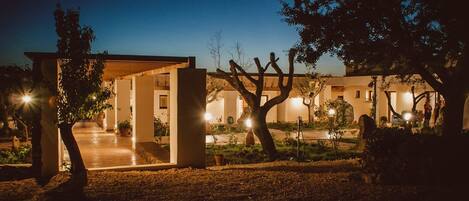 Un edificio moderno con un espacio exterior cubierto, rodeado de árboles e iluminado con luz ambiental.