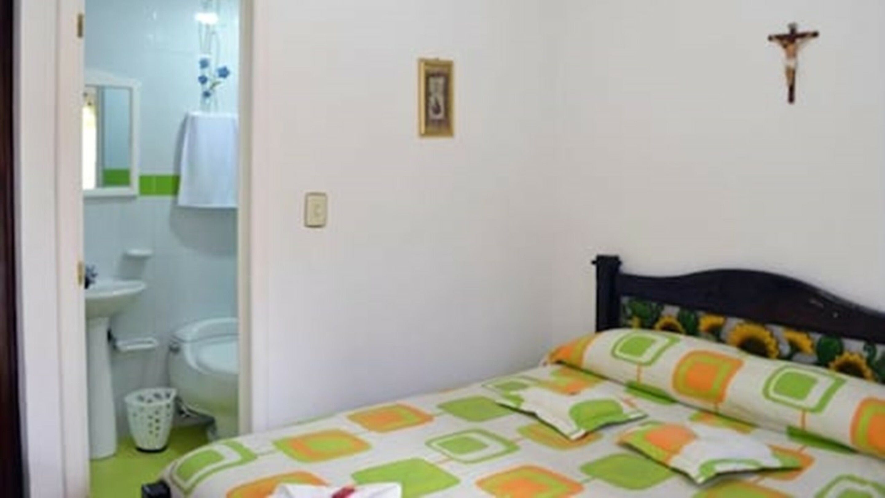 A bedroom with a bed, a wall-mounted cross, and a bathroom visible through an open door.