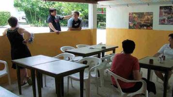 Un área de comedor informal con mesas y sillas, techo cubierto y vistas a zonas verdes.