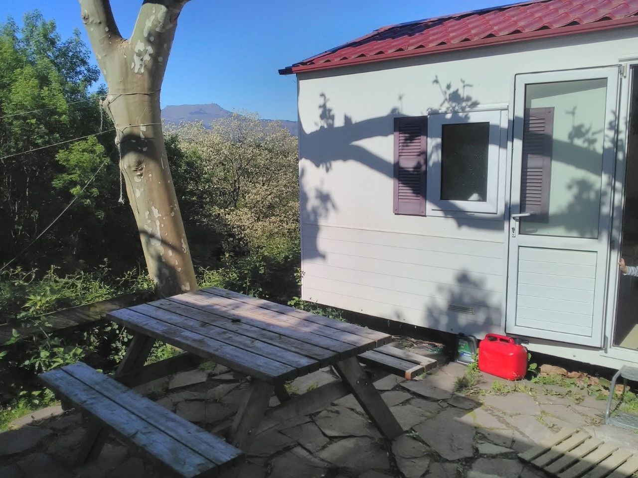 Eine kleine Holzhütte mit einem Picknicktisch und einem roten Gasbehälter davor.