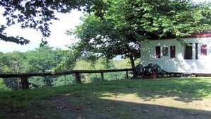A rustic cabin with a wooden fence, surrounded by lush greenery and trees. - Camping Manex - Mobil-Home (Saint-Pee-sur-Nivelle)
