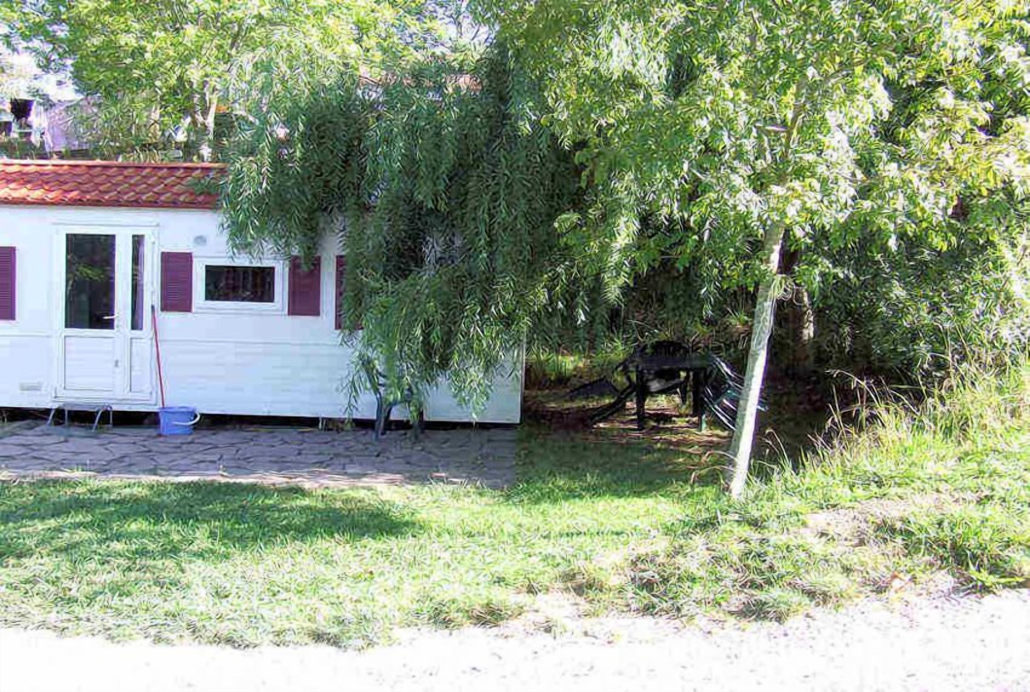 Uma casa móvel pequena e branca com teto vermelho, rodeada por árvores e um espaço gramado.