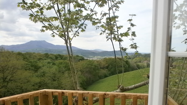 Una terraza de madera con vistas a un exuberante valle verde y montañas distantes.