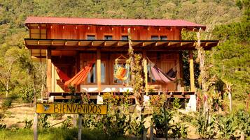 A wooden cabin with a red roof, a hammock, and a 'BIENVENIDOS' sign.