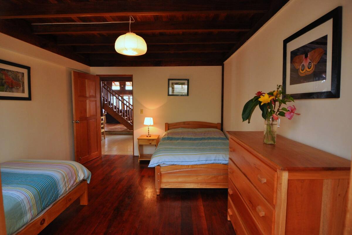 A bedroom with two wooden beds, a nightstand with a lamp, a dresser, and a wooden ceiling.