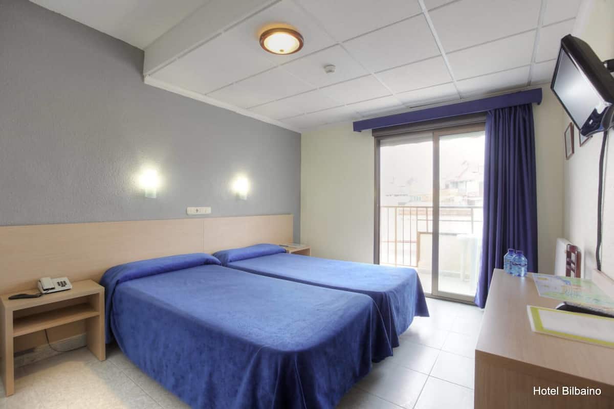 A hotel room with two beds, a desk, a chair, a TV, and a window with a view.