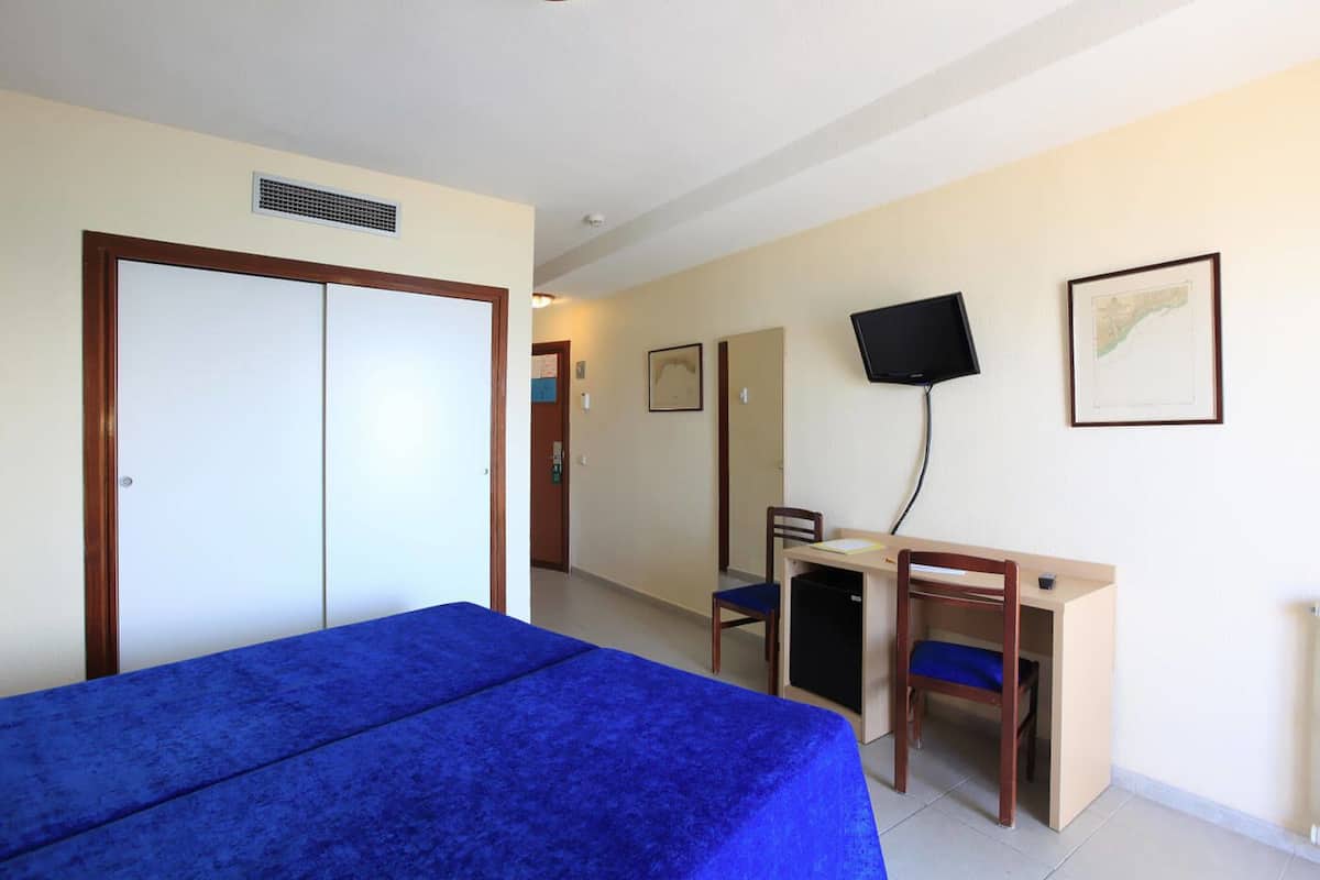 A hotel room with a bed, a desk with a chair, a television, and a door.
