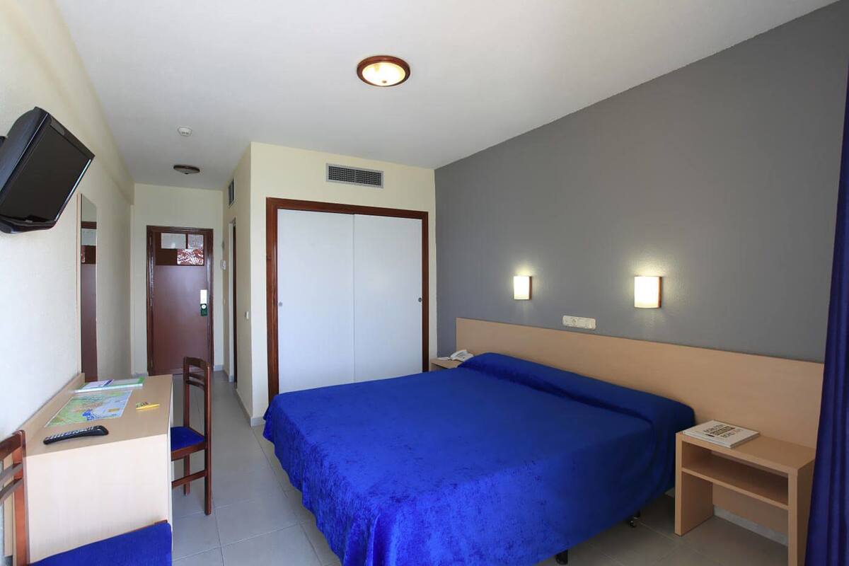 A hotel room with a bed, a desk with a chair, a television mounted on the wall, and two bedside lamps.