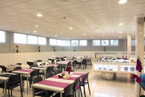 A spacious dining area with multiple tables and chairs, a buffet counter, and large windows providing natural light. - Hotel Bilbaino (Benidorm)