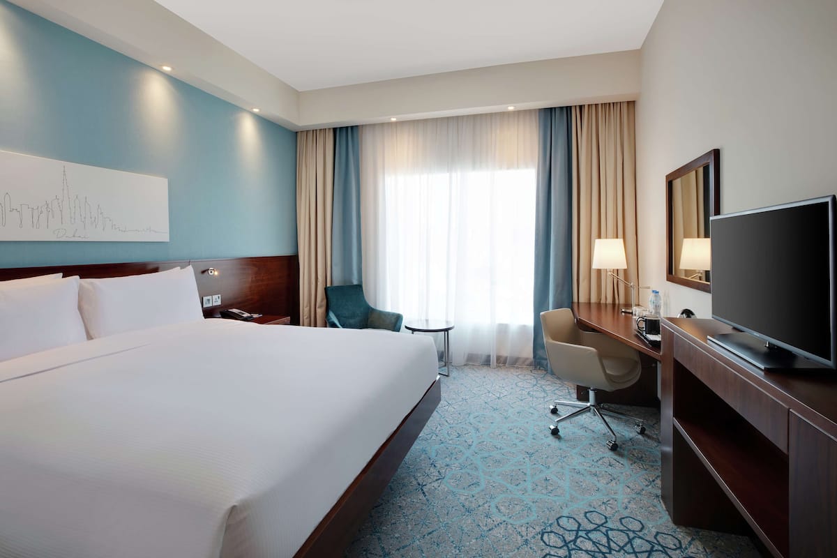 Una habitación de hotel con una cama grande, un escritorio, una silla, un televisor y una ventana con cortinas.