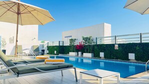 Zona junto a la piscina con sillones de descanso, una mesa y una sombrilla grande.