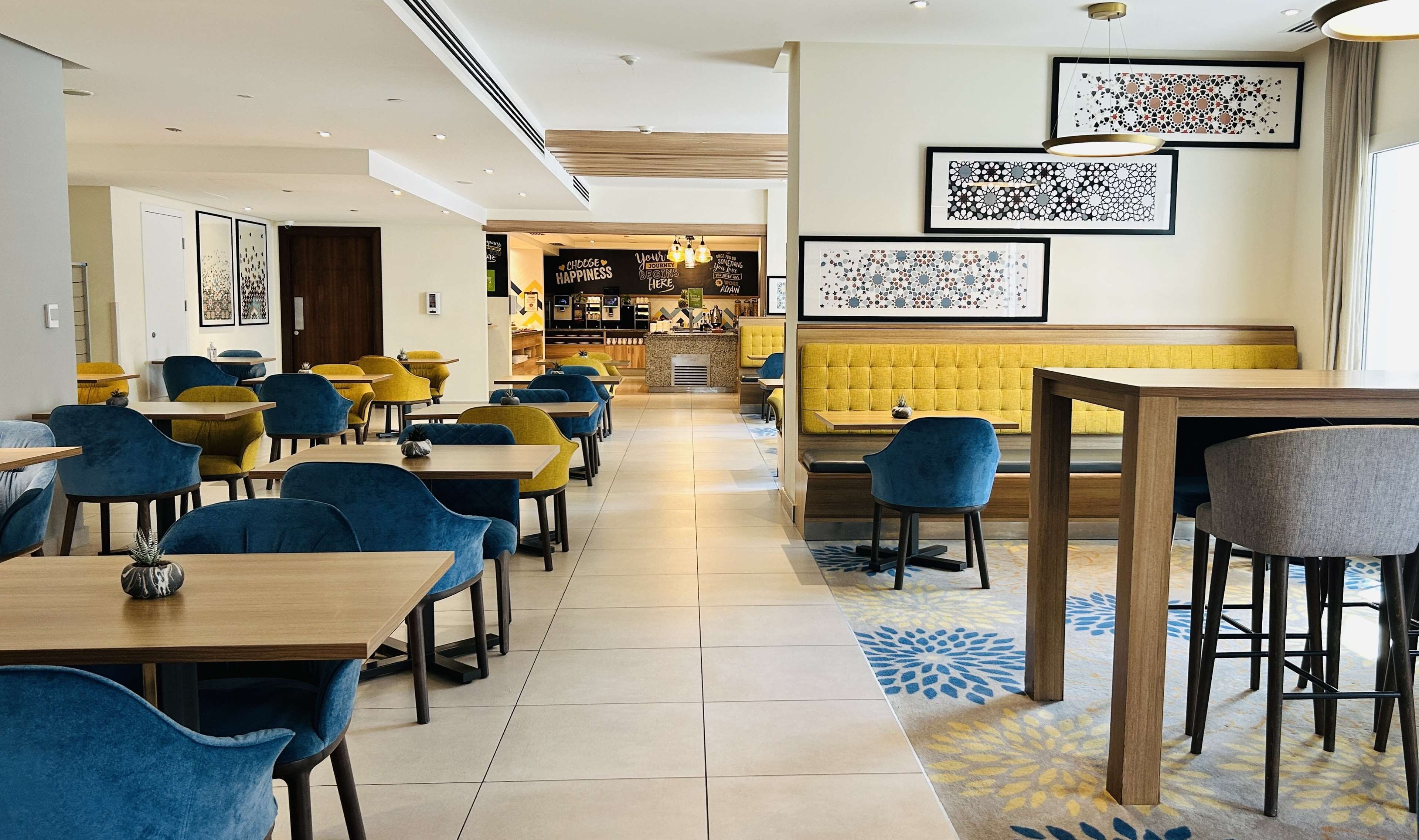 Un restaurant moderne avec des chaises bleues et jaunes, un coin salon jaune et des œuvres d’art encadrées accrochées aux murs.