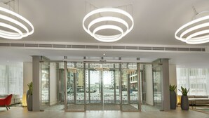 Un moderno vestíbulo de hotel con entrada de vidrio, lámparas circulares en el techo y vistas a la calle.