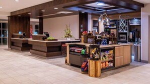 A modern coffee shop with a wooden counter, a refrigerated section, and a variety of snacks and beverages. - Hilton Garden Inn Kansas City Airport (Kansas City)