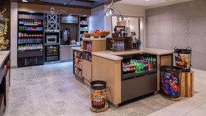 A coffee shop interior with a counter, beverage dispensers, and a display of snacks. - Hilton Garden Inn Kansas City Airport (Kansas City)