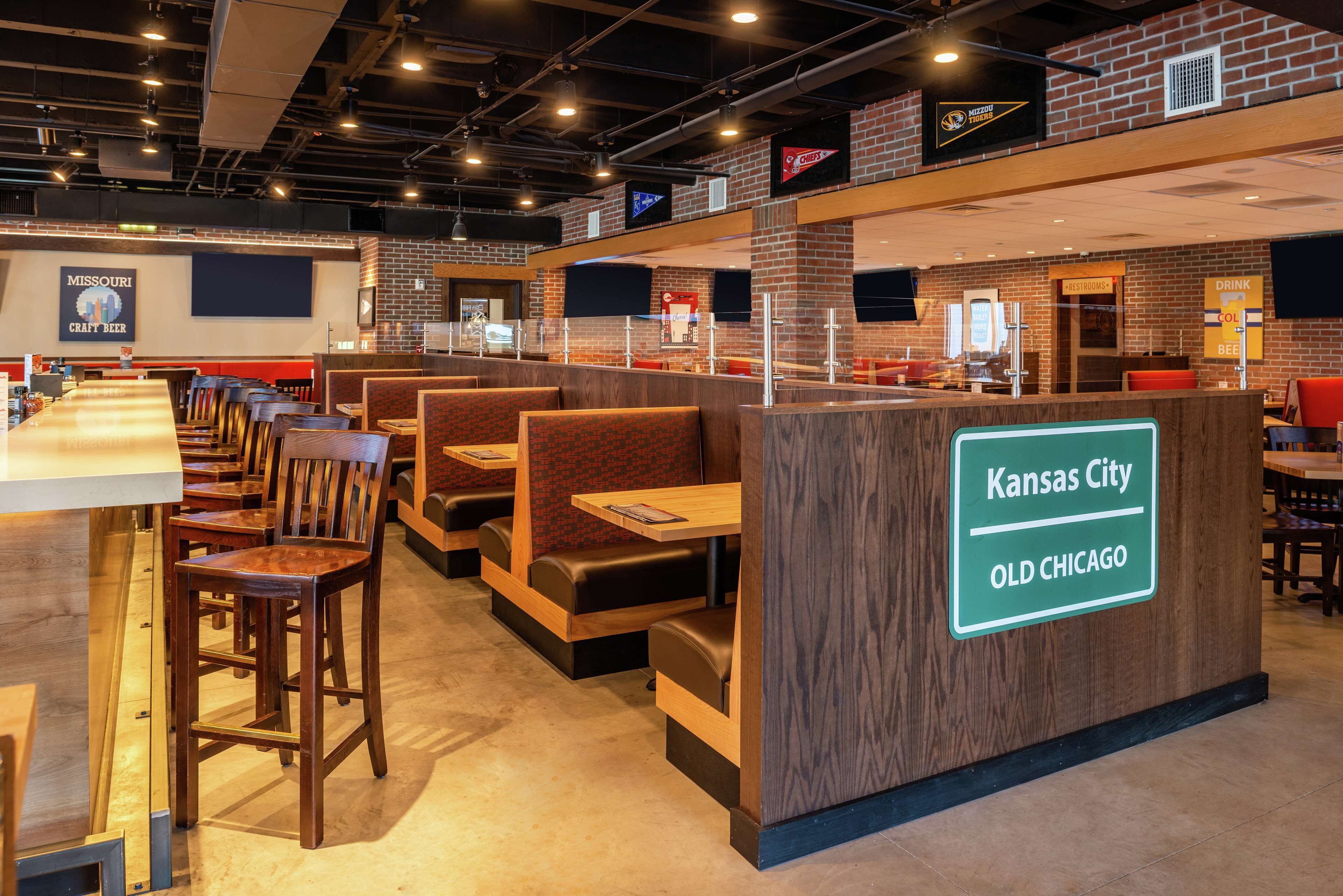 Interior de un restaurante con cabinas y mesas, una barra con un letrero que indica Kansas City, Old Chicago y una pizarra de menú.