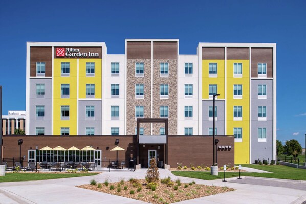 A multi-story hotel with a modern design, featuring a mix of yellow and grey facades, and a visible entrance with outdoor seating.