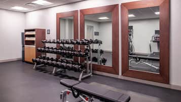 Un gimnasio con equipo de levantamiento de pesas, bancos y un espejo grande.
