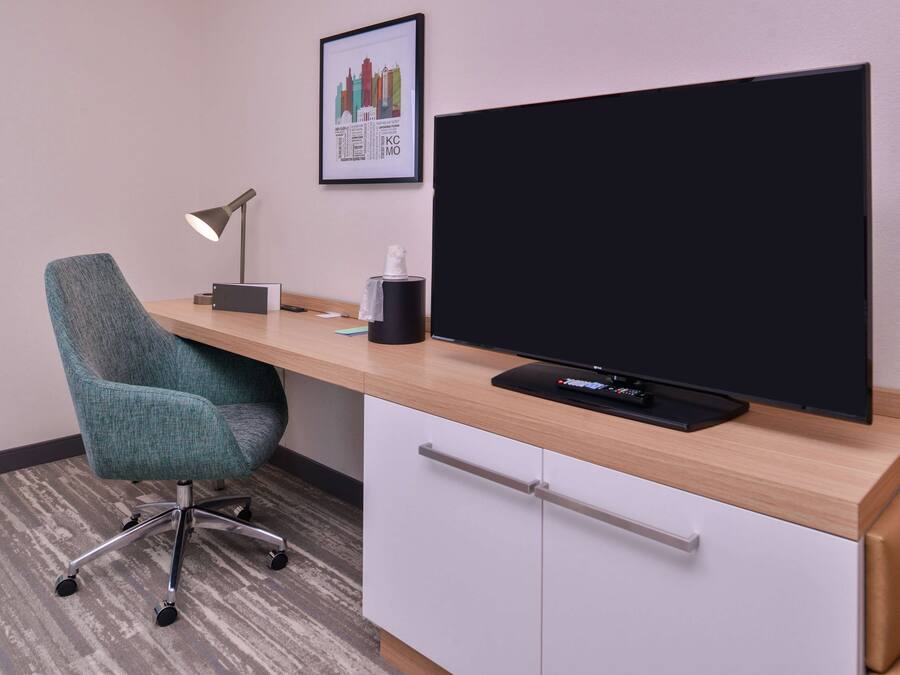 Un escritorio moderno con un televisor de pantalla plana, una silla de oficina color turquesa, una lámpara de escritorio y una caja de pañuelos.