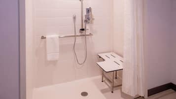 Un moderno espacio de ducha con un cabezal de ducha de mano, un panel de control montado en la pared y un pequeño banco blanco.