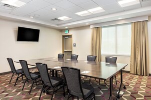 Un salón de conferencias con una larga mesa, seis sillas, un televisor de pantalla plana, un letrero de salida y una ventana con cortinas.