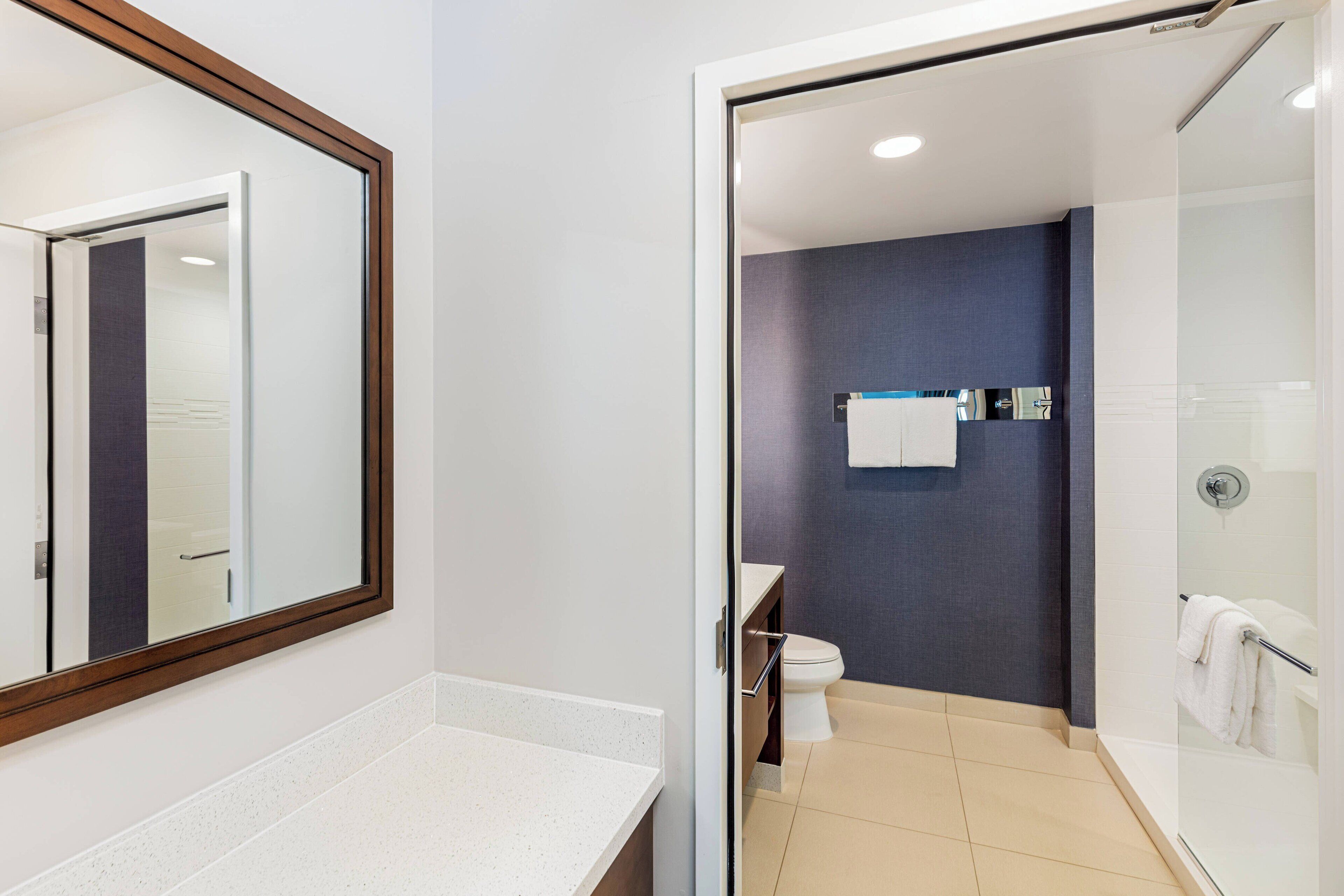 A modern bathroom with a white countertop, a glass shower enclosure, and a dark blue wall.